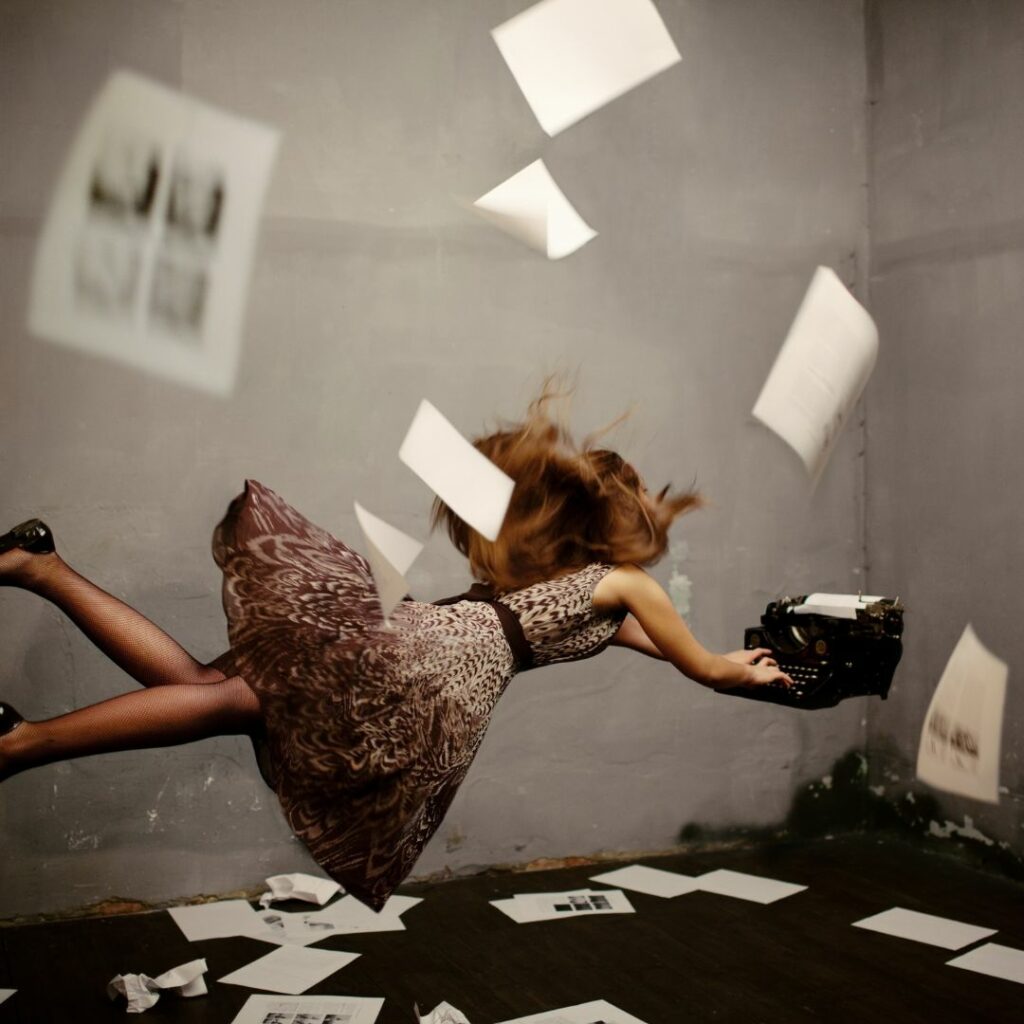 Eine Frau scheint in einem Zimmer waagrecht in der Luft zu schweben. Sie tippt auf einer Schreibmaschine während Papierseiten um sie herum fallen.