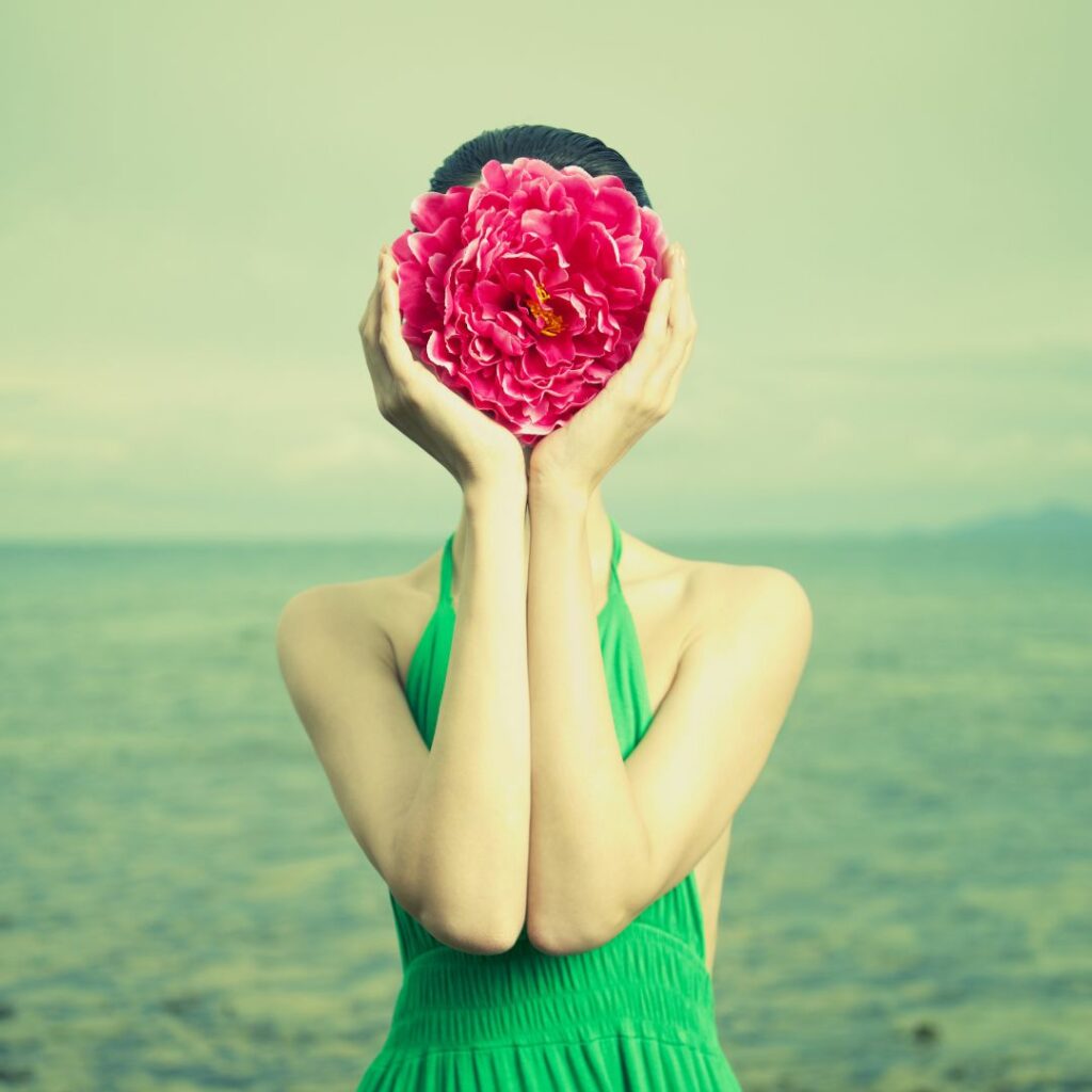 Eine Frau in grünem Kleid hält sich eine riesige Blüte vor ihr Gesicht.
