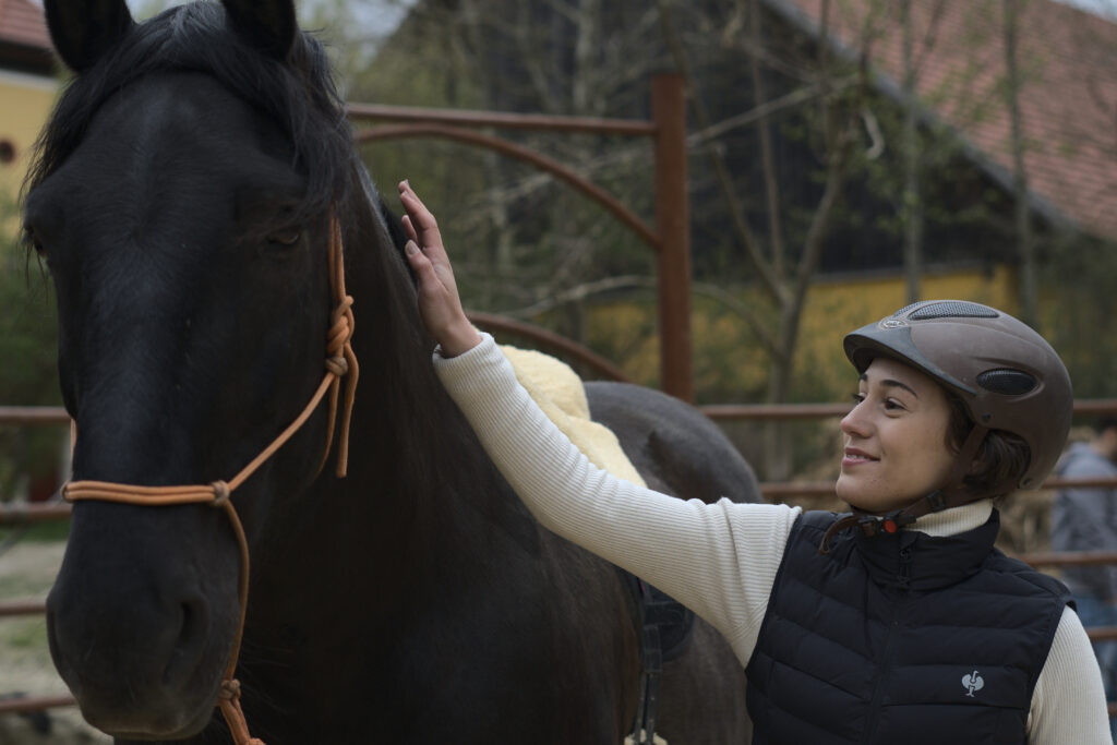 Eine Frau legt zärtlich ihre Hand auf den Hals eines schwarzen Pferdes und blickt es liebevoll an.