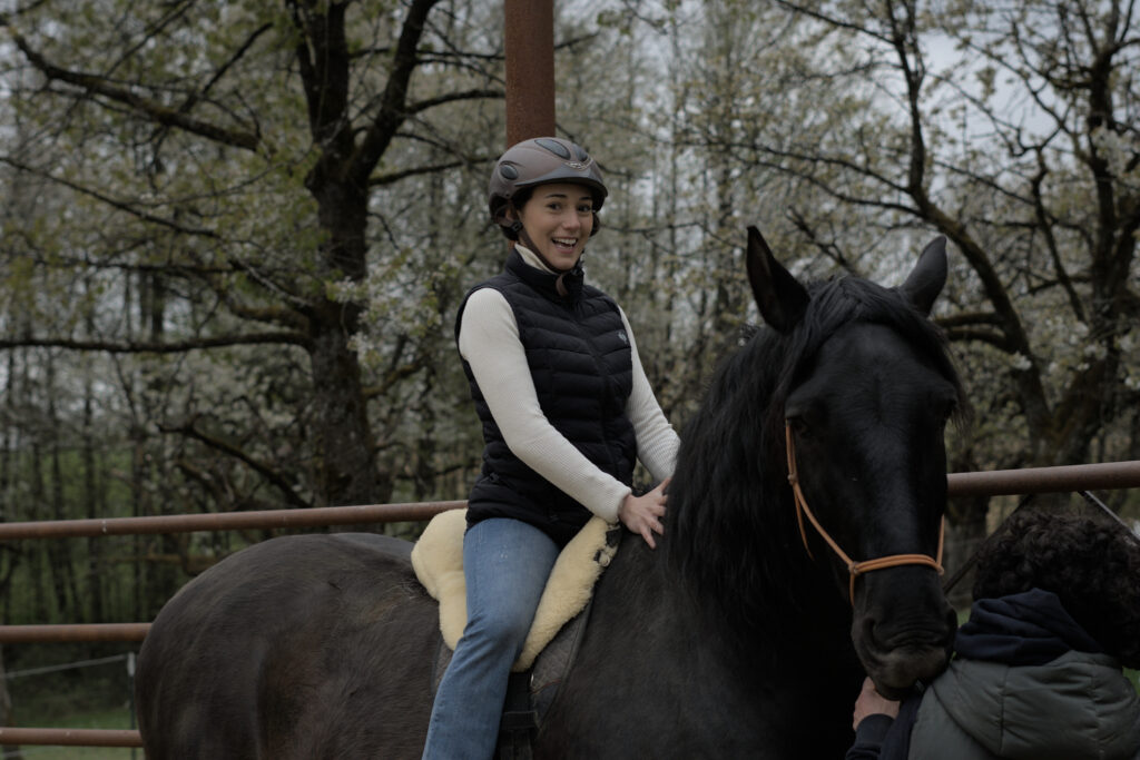 Eine junge Frau sitzt mit begeistertem Gesicht auf einem großen schwarzen Pferd.