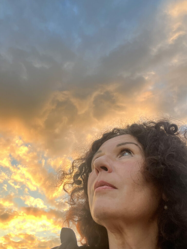 Frau schaut in einen von Sonne durchschienenen Wolkenhimmel hoch
