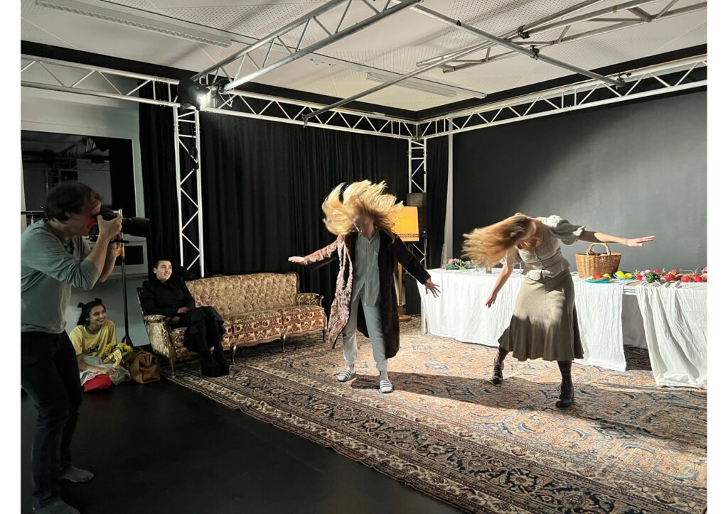 Zwei Schauspielschülerinnen tanzen, ein Mann fotografiert sie und zwei andere Schülerinnen schauen zu.