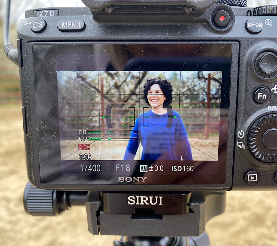 Blick auf das Display einer Filmkamera, in dem man eine lächelnde Frau mit blauem Pullover sieht.