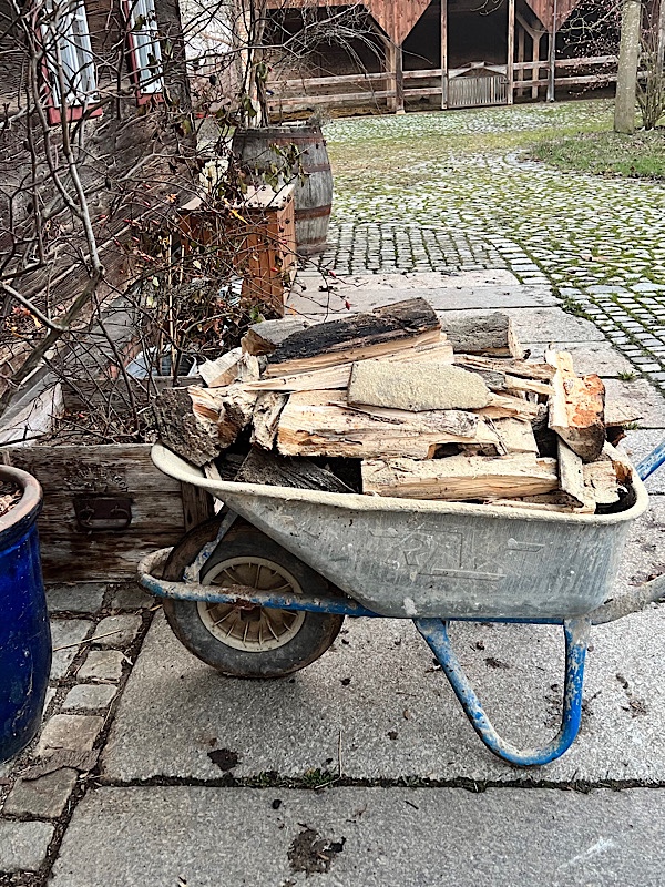Eine Schubkarre mit gehacktem Holz in einem gepflasterten Innenhof.