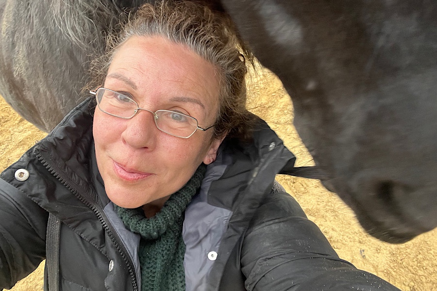Eine Frau mit Pferd im Hintergrund macht ein Selfie